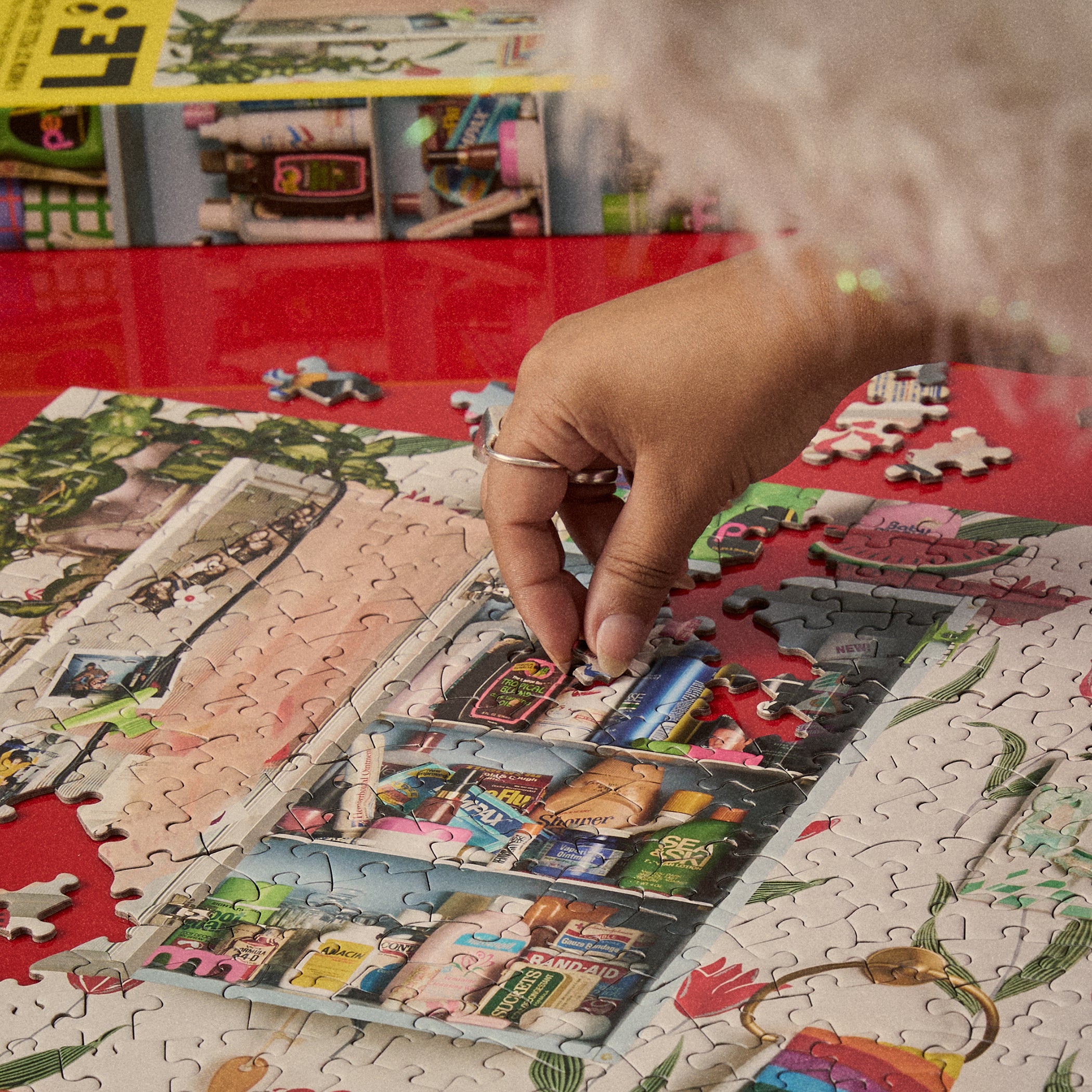 Hand placing a piece into the Le Puzz Too-Da-Loo 500 piece jigsaw puzzle on a red table with box in background