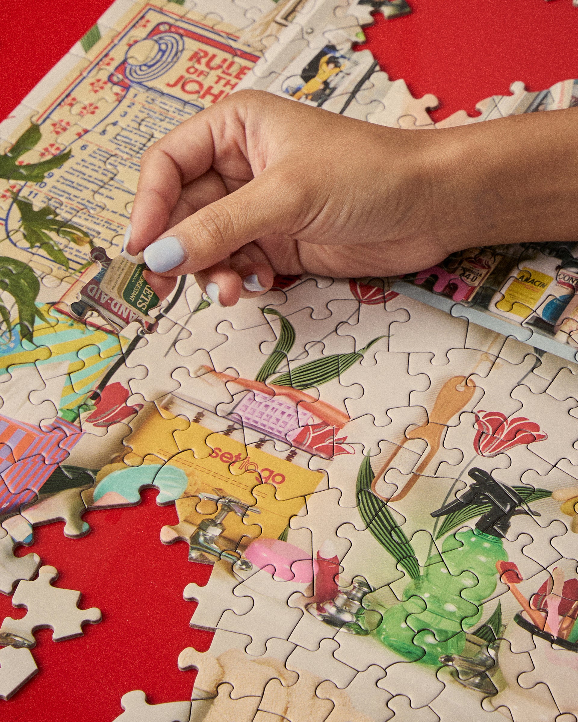 Close-up of hand placing a piece into the Le Puzz Too-Da-Loo 500 piece jigsaw puzzle on a red surface