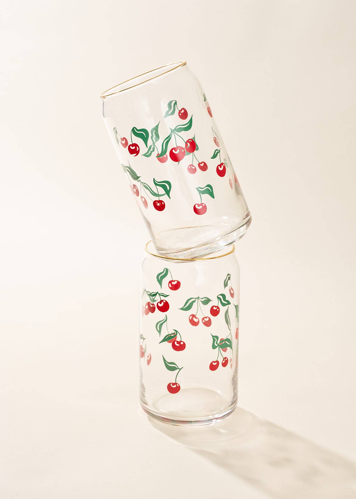Two glass tumblers with cherry pattern stacked on a light background