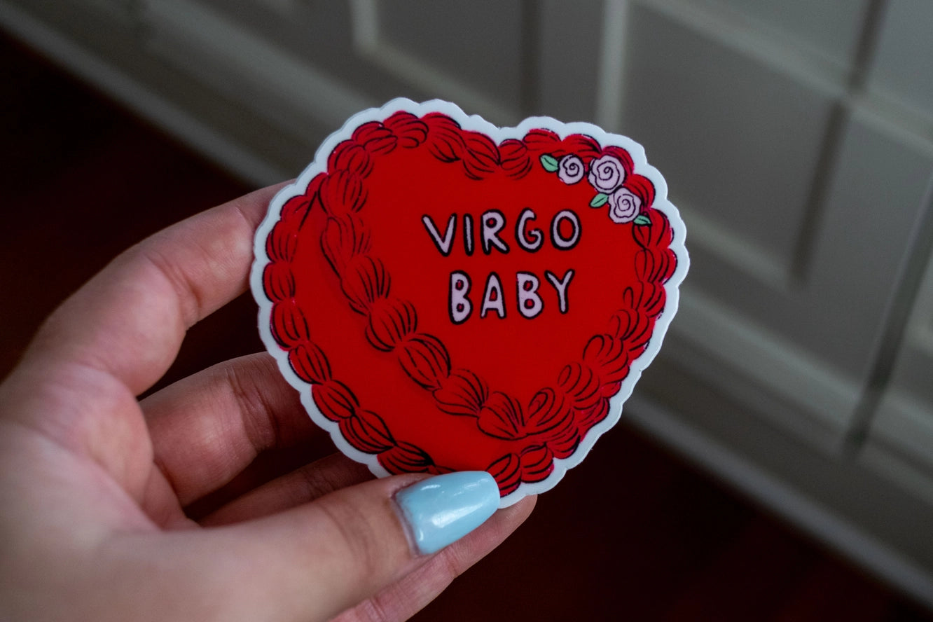 Hand holding a red 'Virgo Baby' sticker with floral designs.