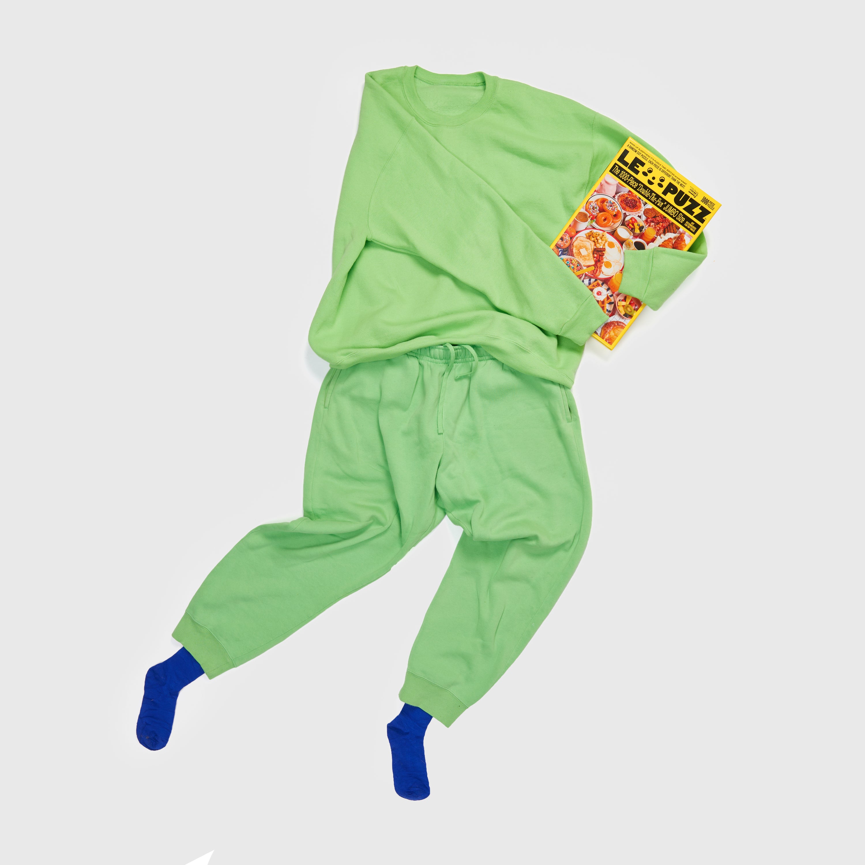 Le Puzz Wakey Wakey puzzle box styled with a green sweatsuit and blue socks on a white background