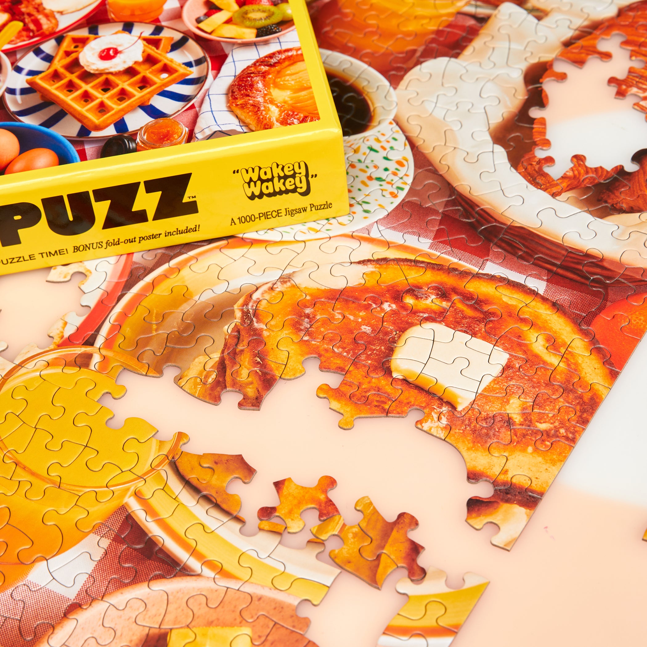 Le Puzz Wakey Wakey yellow puzzle box beside partially assembled breakfast puzzle pieces on a pink surface