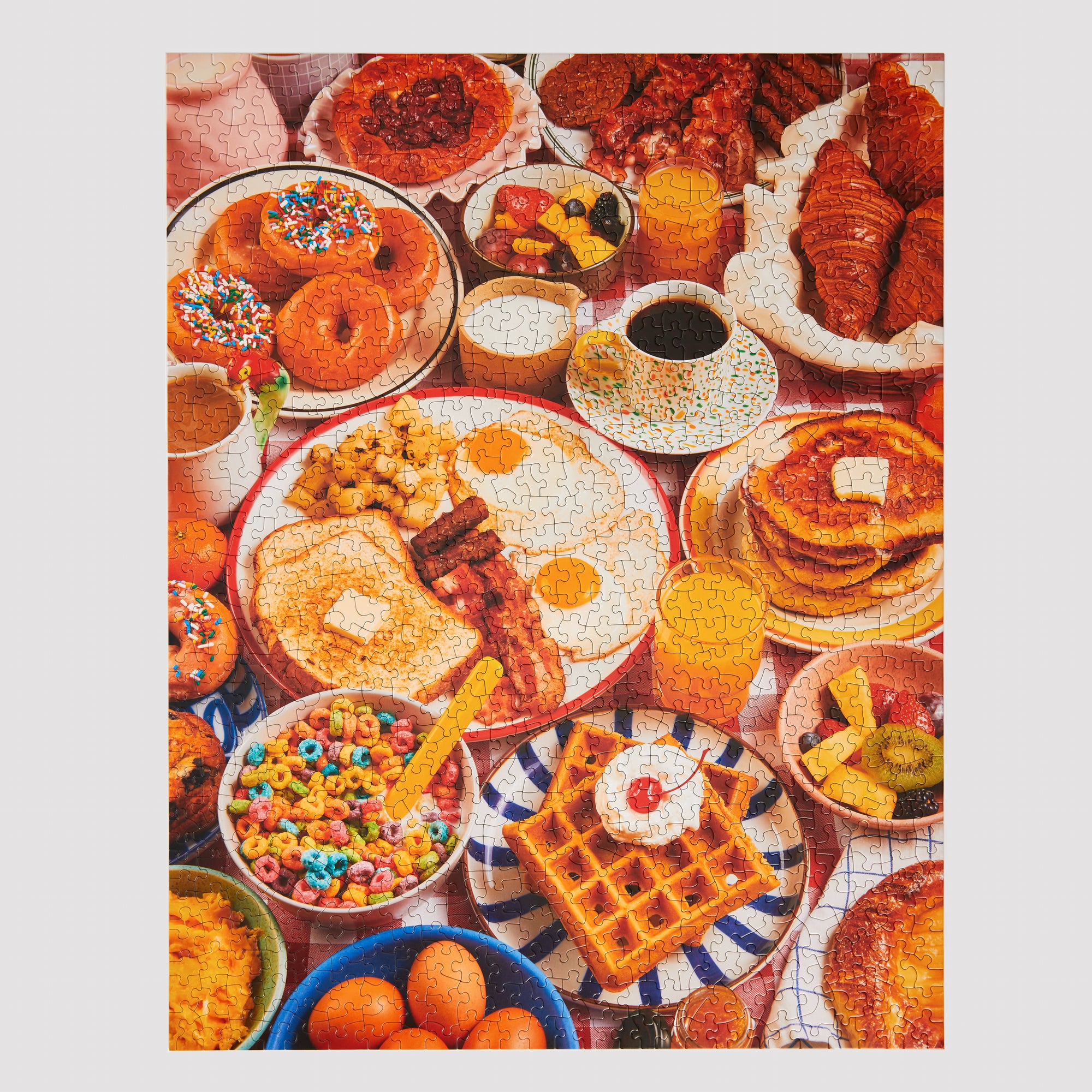 Completed Le Puzz Wakey Wakey 1000-piece jigsaw puzzle showing a vibrant overhead breakfast spread with donuts, waffles, eggs, cereal, and croissants