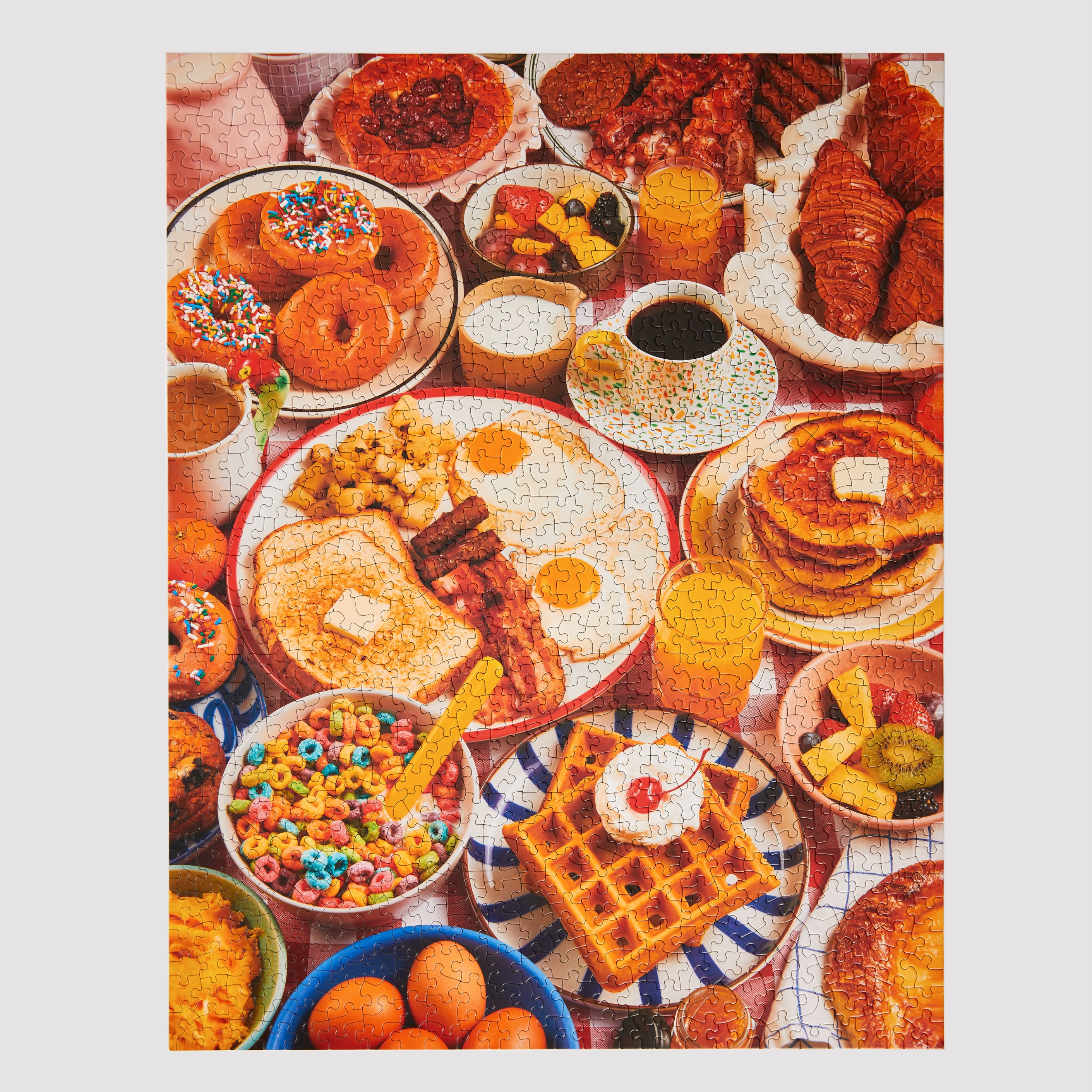 Completed Le Puzz Wakey Wakey 1000-piece jigsaw puzzle showing a vibrant overhead breakfast spread with donuts, waffles, eggs, cereal, and croissants