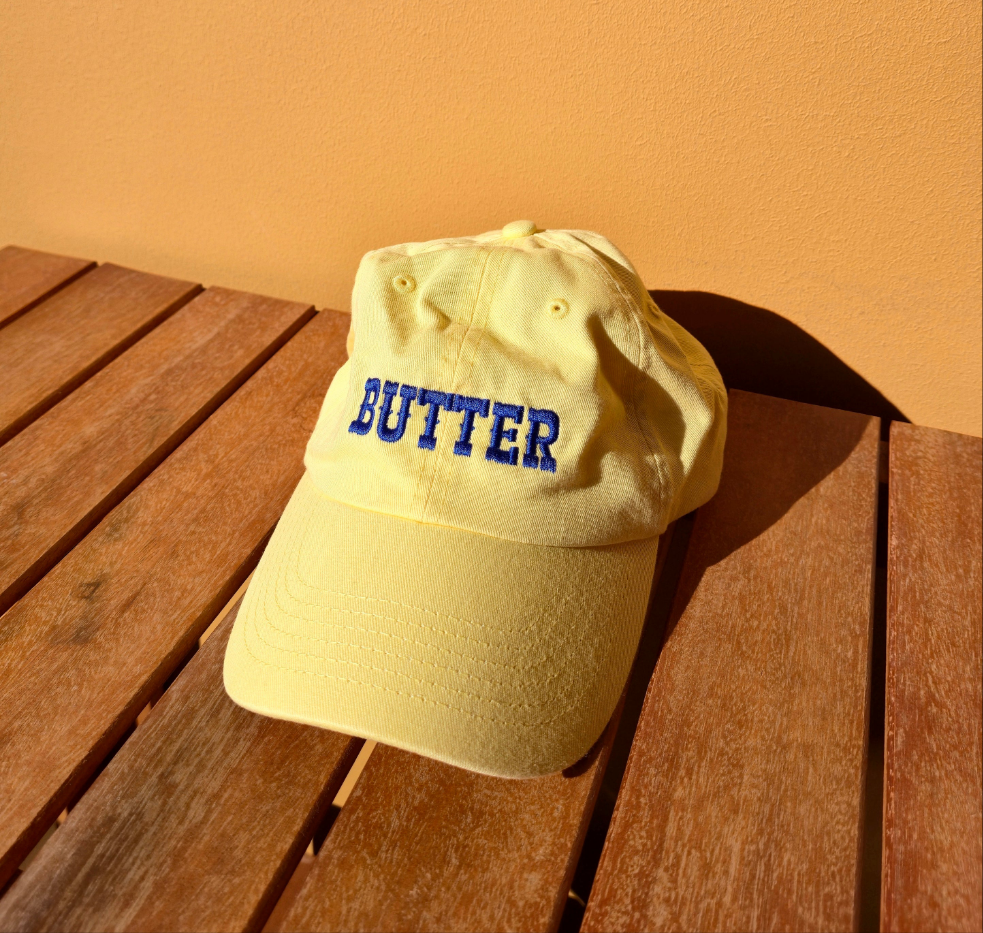 Yellow cap with 'BUTTER' text on a wooden surface against an orange wall