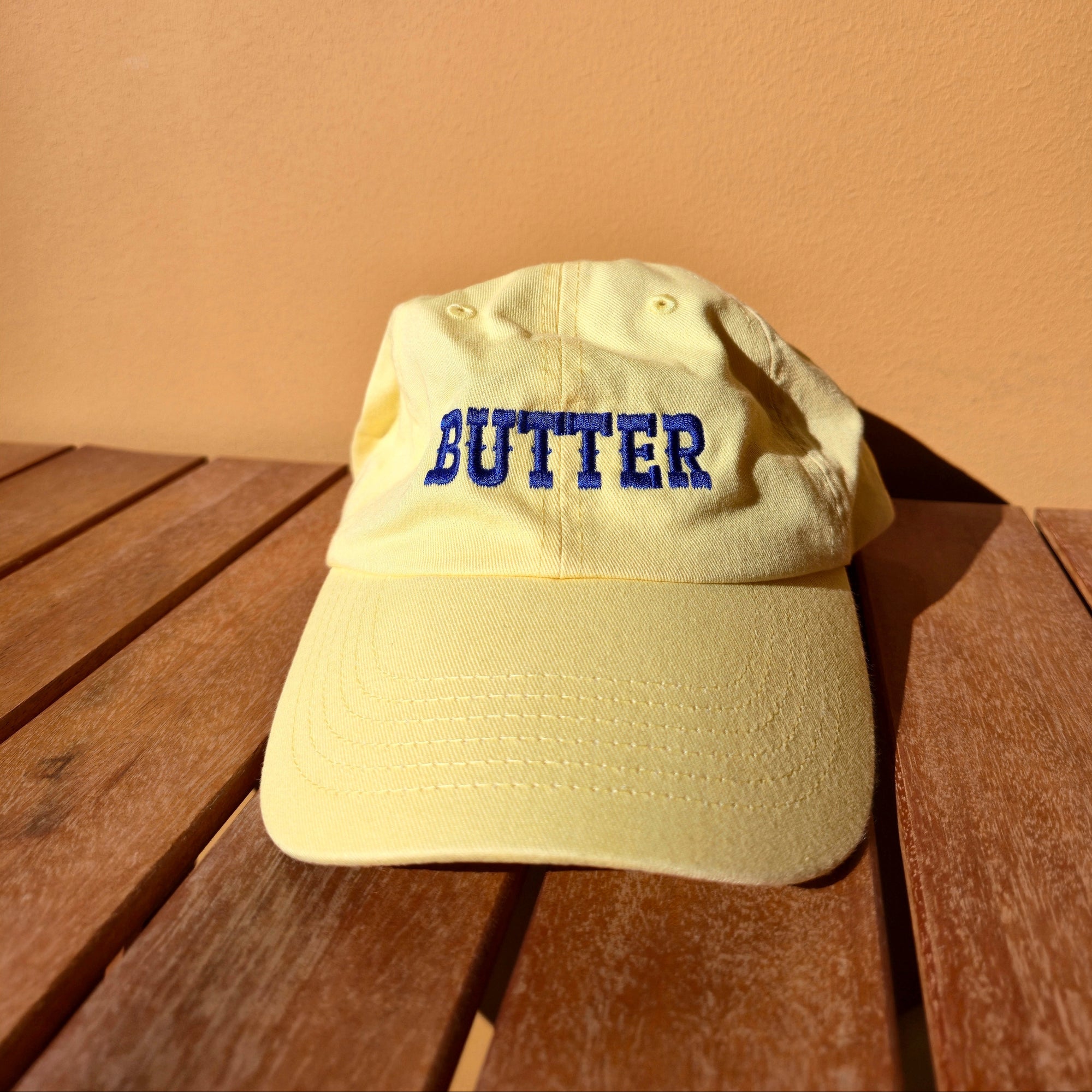 Beige cap with 'BUTTER' text on a wooden surface